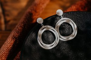 Silberfarbene Ohrhänger mit rundem Stecker und mehreren überlappenden Kreiselementen in matter Optik, dekorativ auf einer schwarzen Schale präsentiert.