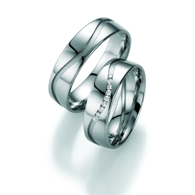 Elegantes Partnerring-Set in Silberoptik mit geschwungenem, mattiertem Designelement auf hochglanzpolierter Oberfläche. Einer der Ringe ist mit einer Reihe funkelnder klarer Zirkonia-Steine besetzt und verleiht dem Set eine edle, moderne Ausstrahlung. Ideal als Trau-, Verlobungs- oder Freundschaftsringe.