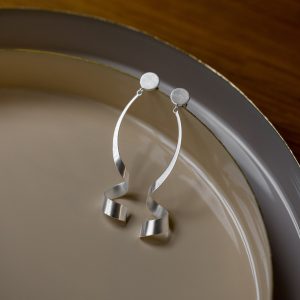 Silberfarbene Ohrhänger mit runden Ohrsteckern und elegant geschwungenen, spiralartigen Anhängern in matter Optik, dekorativ auf einem Teller präsentiert.
