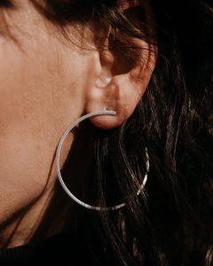 Silberfarbene offene Creole in matter Optik, getragen am Ohr und detailreich in Nahaufnahme dargestellt.