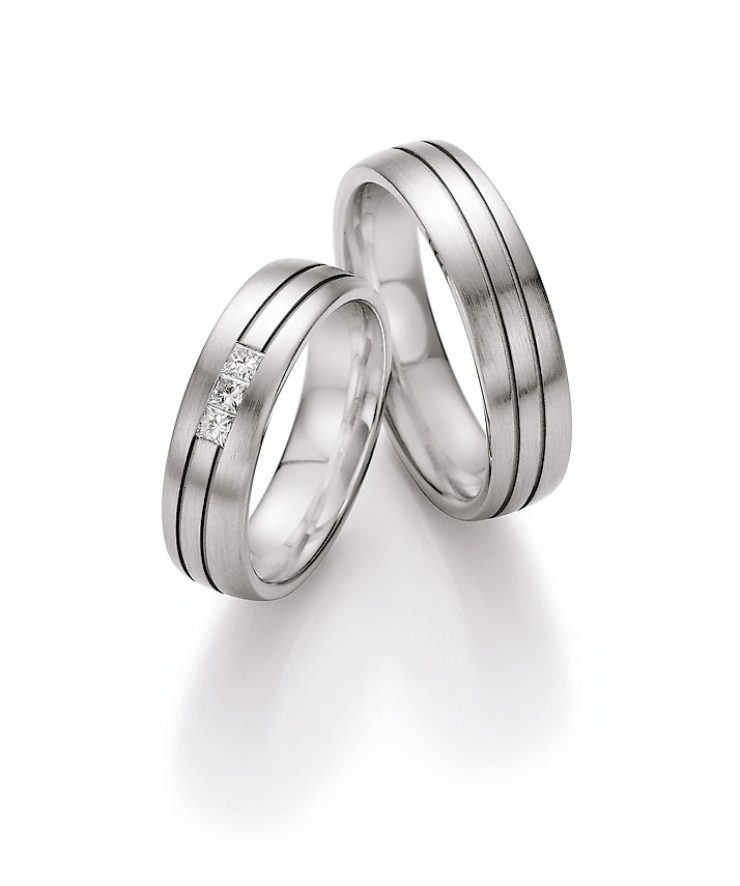 Zeitloses Trauring-Set in eleganter Silberoptik mit fein mattierter Oberfläche und dezenten, umlaufenden Zierlinien. Der Damenring wird durch drei quadratisch gefasste Diamanten stilvoll veredelt und setzt einen modernen, funkelnden Akzent. Die klare Formensprache und das harmonische Design machen diese Ringe zu einem besonderen Symbol für Liebe, Treue und Beständigkeit.