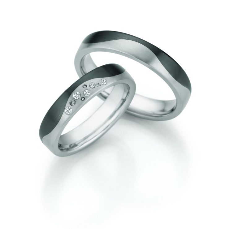 Elegantes Trauring-Set in moderner Titanoptik mit harmonisch geschwungenem Design in mattierten und polierten Oberflächen. Der Damenring wird durch mehrere funkelnde Diamanten stilvoll veredelt, während der Herrenring die klare Linienführung aufgreift. Eine ausdrucksstarke Kombination aus zeitgemäßer Ästhetik, Beständigkeit und symbolischer Verbundenheit.