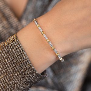 Schmaler zweifarbiger Armreif mit funkelnden Zirkonia-Steinen am Handgelenk einer Person in glitzerndem Oberteil.
