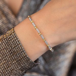 Schmaler zweifarbiger Armreif mit funkelnden Zirkonia-Steinen am Handgelenk einer Person in glitzerndem Oberteil.