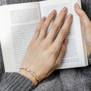Hand mit dezentem zweifarbigem Armband und Sternanhängern liegt auf einem aufgeschlagenen Buch mit italienischem Text.