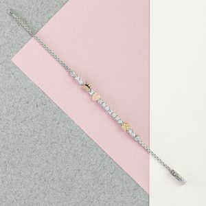Silbernes Armband mit Herz-, Pfoten- und Blumenmotiven sowie funkelnden Schmuckelementen auf rosa und grauem Hintergrund.