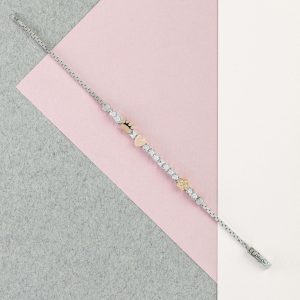 Silbernes Armband mit Herz-, Pfoten- und Blumenmotiven sowie funkelnden Schmuckelementen auf rosa und grauem Hintergrund.