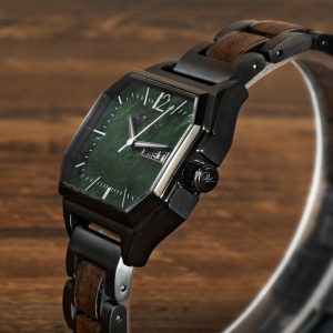 Waidzeit Armbanduhr mit schwarzem achteckigem Gehäuse, grünem Zifferblatt, Wochentags- und Datumsanzeige und schwarzem Metallarmband mit dunklen Holzeinlagen, dargestellt auf einer Holzoberfläche