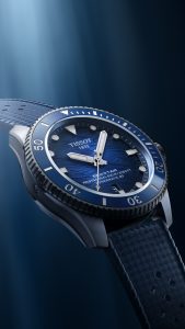 Tissot Seastar 1000 Powermatic 80 mit blauem Zifferblatt in Wellenoptik, drehbarer Taucherlünette und blauem Kautschukarmband. Dynamische Produktaufnahme der professionellen Taucheruhr mit Wasserdichtigkeit bis 600 Meter.