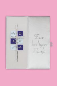 Aufgeschlagenes Buch mit silberner Kreuzapplikation und gesticktem Schriftzug 'Zur heiligen Taufe' auf weißem Einband vor rosa Hintergrund