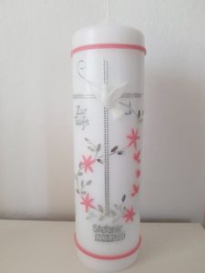 Weiße Kerze mit silbernem Kreuz, rosa Blumenornamenten und lesbarer Aufschrift.
