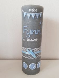 Zylindrische Kerze mit blauer Schleife, Spitzenband, christlichen Symbolen und der Aufschrift 'Meine TAUFE Fynn 30.06.2019'.